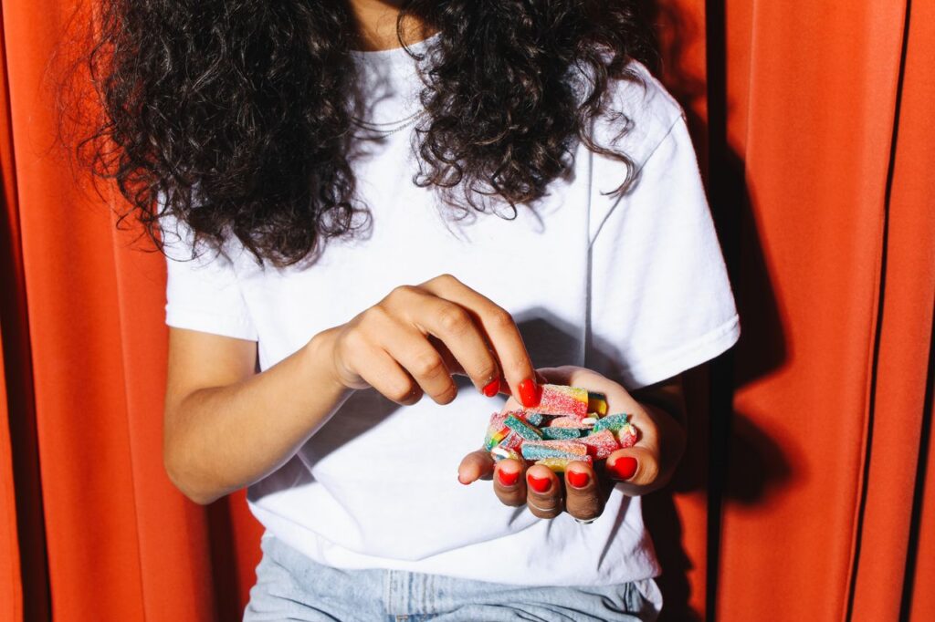 A person in casual attire holding colorful gummy candies against a red curtain backdrop.
